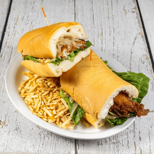 Two Cuban sandwiches with fried fish, lettuce, and onions, served with shoestring fries.