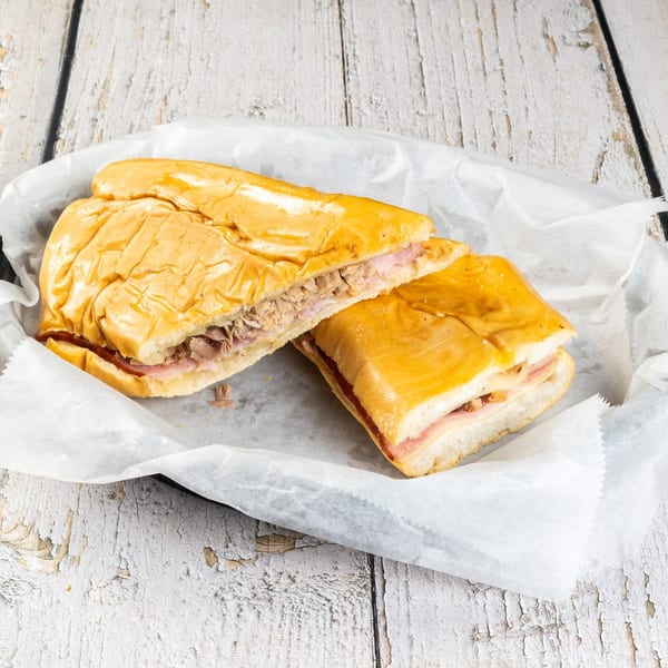 Two halves of a Cuban sandwich with ham, cheese, and roasted pork on a white paper-lined tray.