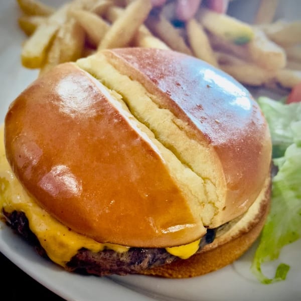 Cheeseburger with melted cheese, a golden bun, and a side of french fries and lettuce.