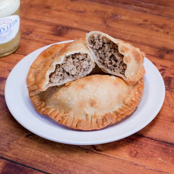 Two golden-brown Cuban beef empanadas, one cut open to show the savory ground meat filling, on a white plate.