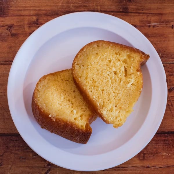 Two slices of golden Cuban pound cake on a white plate, against a rustic wooden table.