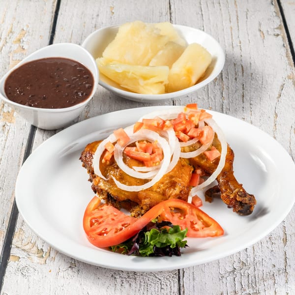 Cuban roasted chicken with onions, tomatoes, black beans, and yuca on a white plate.