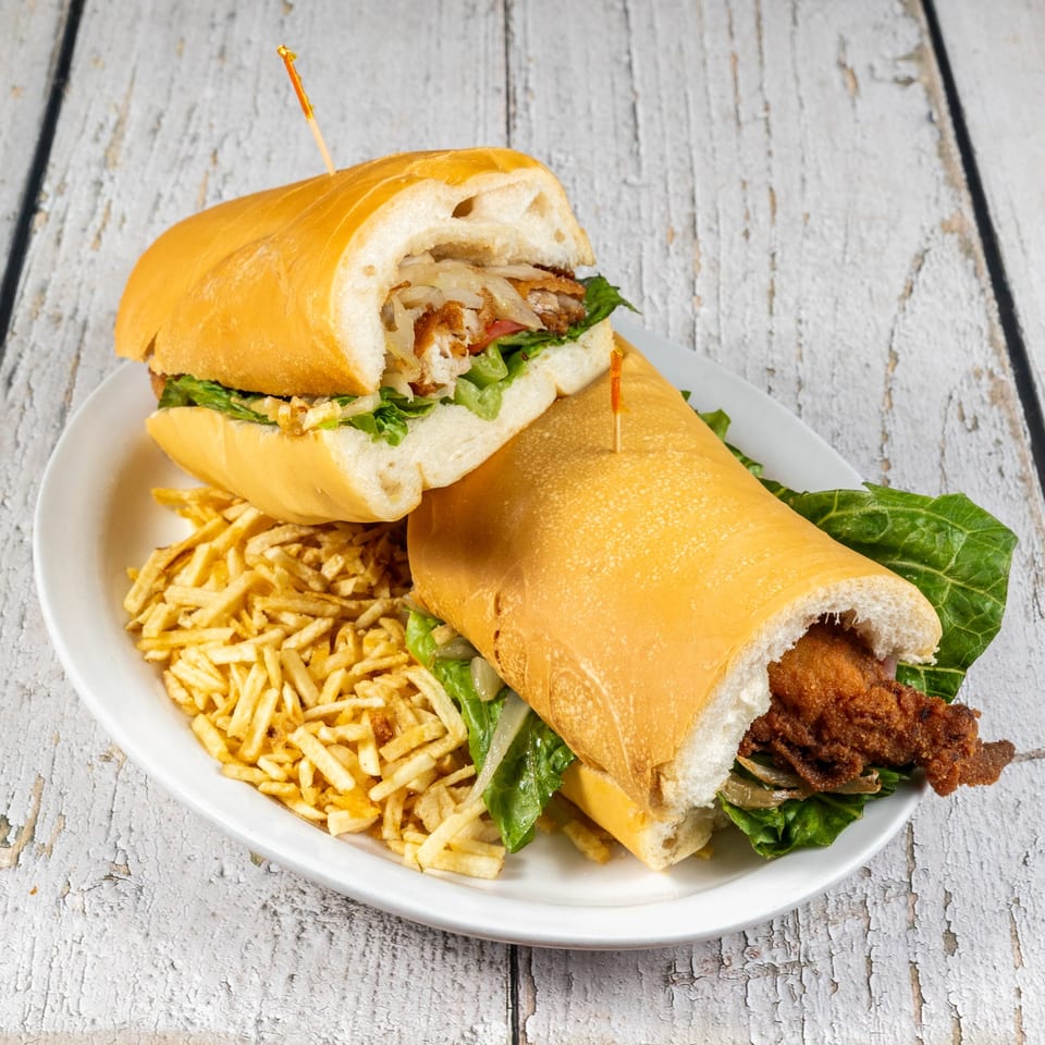 Two Cuban sandwiches with fried fish, lettuce, and onions, served with shoestring fries.