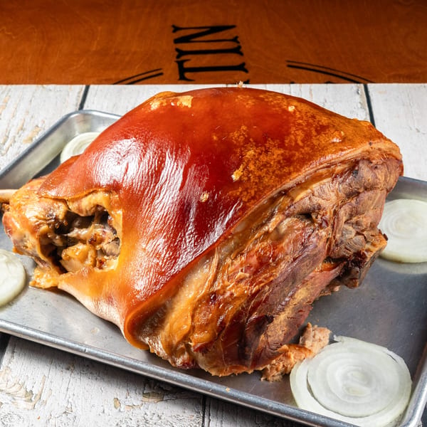 A large, roasted pork shoulder with crispy skin and sliced onions on a metal tray.