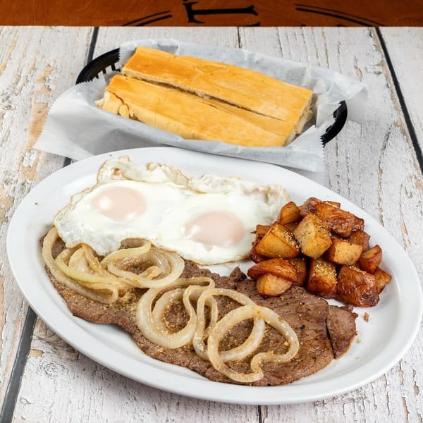 Cuban breakfast with steak, fried eggs, home fries, and onions, served with Cuban bread.